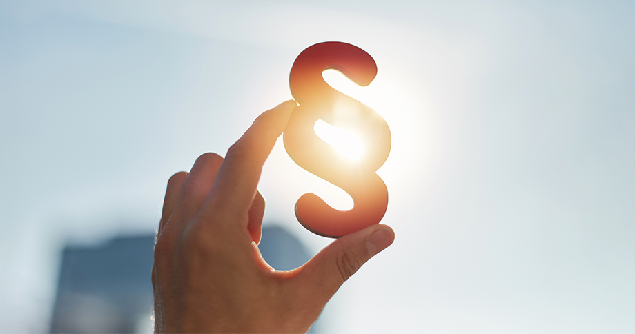Hand hält ein Paragraphenzeichen vor die Sonne als Symbol für die Gesetzesänderung
